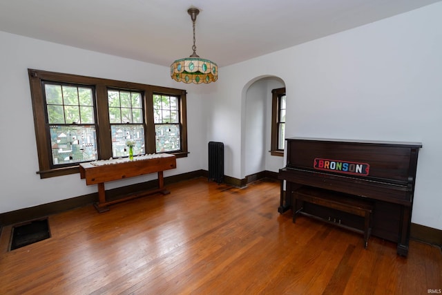living area with radiator heating unit, wood finished floors, arched walkways, and baseboards