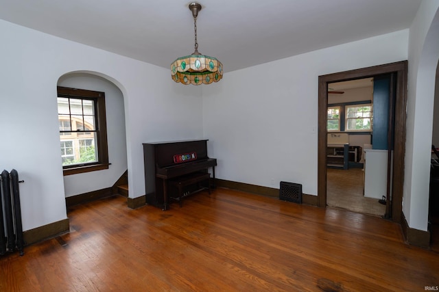 empty room featuring radiator heating unit, wood finished floors, baseboards, and arched walkways