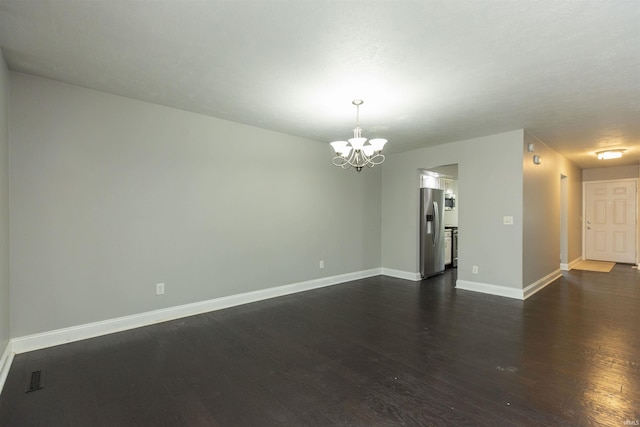 empty room with a chandelier, dark wood finished floors, and baseboards
