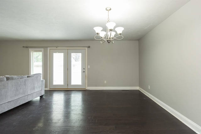 unfurnished living room featuring a chandelier, baseboards, and dark wood finished floors