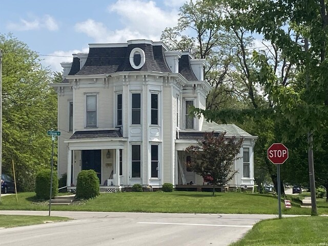 victorian home featuring mansard roof, a front lawn, and a shingled roof