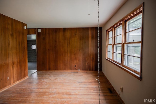 spare room with light wood-style floors, wood walls, and baseboards