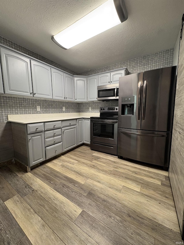 kitchen featuring appliances with stainless steel finishes, gray cabinetry, light wood-type flooring, light countertops, and decorative backsplash