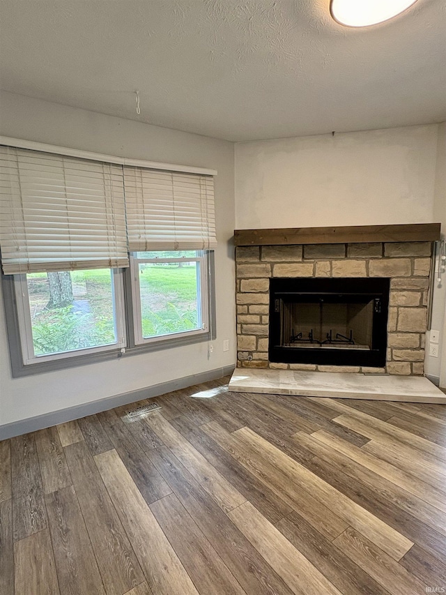 unfurnished living room featuring wood finished floors, a stone fireplace, baseboards, and a textured ceiling