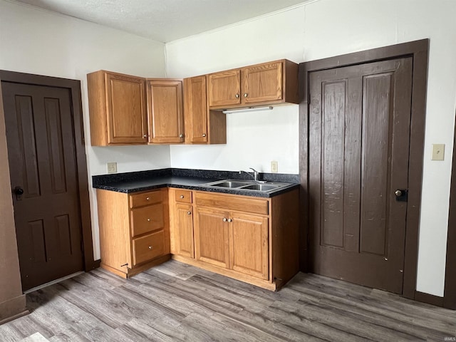 kitchen featuring a sink, light wood-style floors, brown cabinetry, and dark countertops