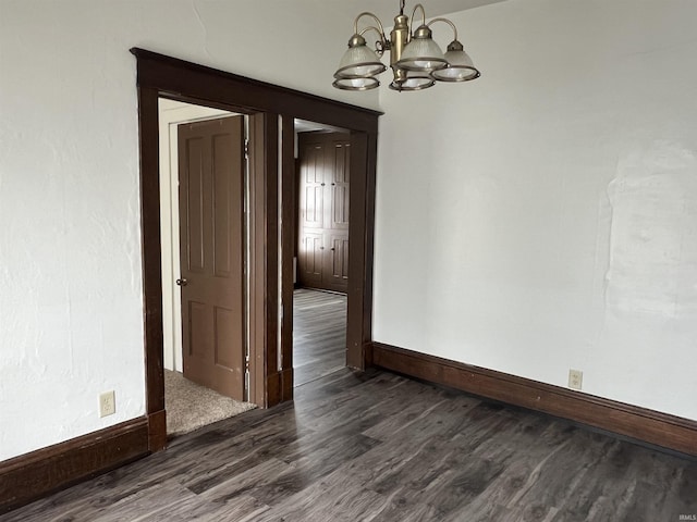 empty room featuring a chandelier, dark wood-type flooring, and baseboards