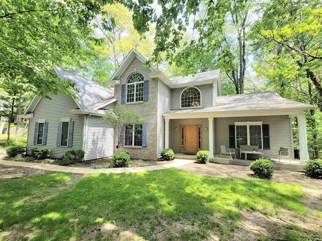 traditional-style house featuring a front lawn, covered porch, and roof with shingles
