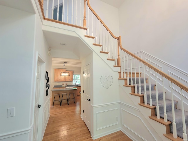 stairway with wood finished floors, a high ceiling, and wainscoting