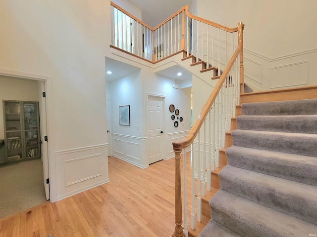 stairs featuring wood finished floors, a towering ceiling, a decorative wall, and wainscoting