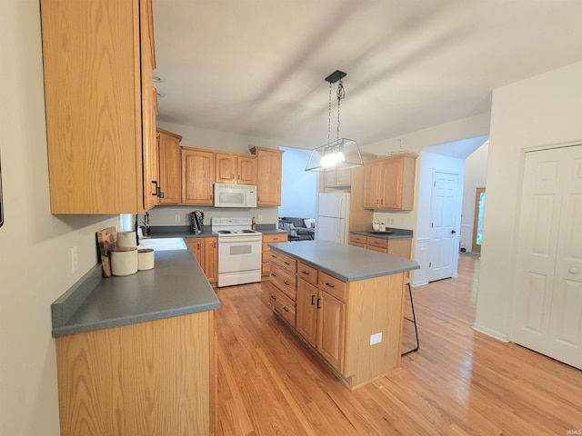 kitchen with white appliances, a center island, dark countertops, and a sink