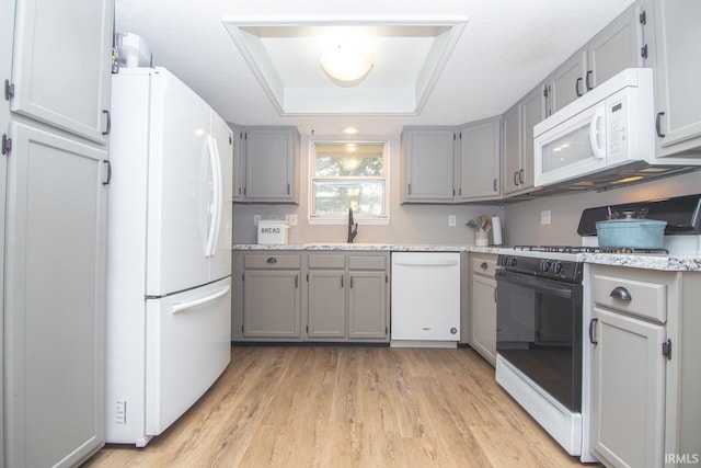 kitchen featuring white appliances, gray cabinetry, light wood finished floors, and a tray ceiling