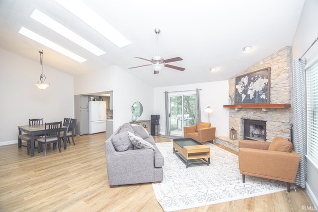 living area with a skylight, light wood finished floors, a stone fireplace, ceiling fan, and high vaulted ceiling