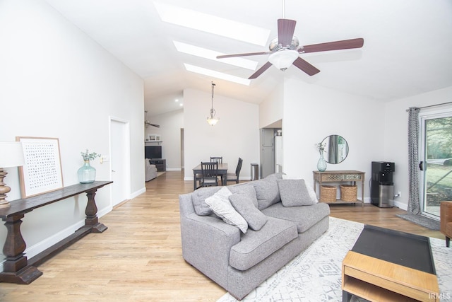 living room with ceiling fan, vaulted ceiling, light wood-style flooring, and a skylight