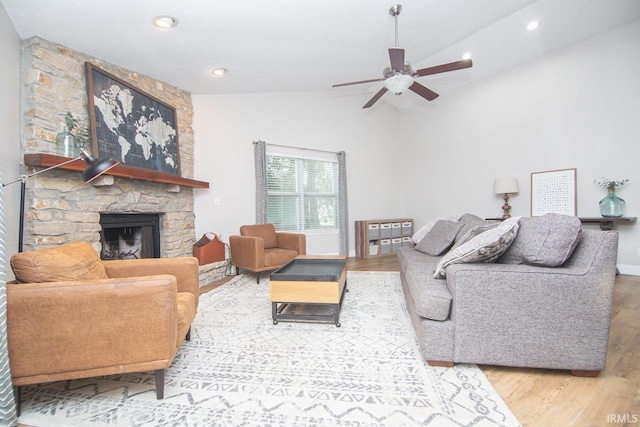 living area featuring lofted ceiling, wood finished floors, a ceiling fan, and a stone fireplace