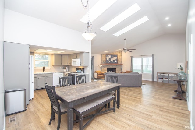 dining space featuring a skylight, healthy amount of natural light, a stone fireplace, ceiling fan, and high vaulted ceiling