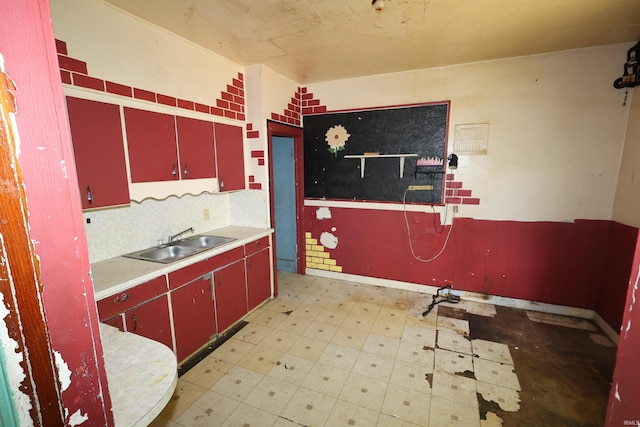 kitchen with red cabinetry, a sink, light flooring, and backsplash