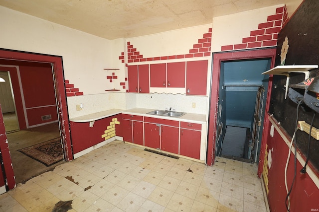 kitchen with red cabinets, light flooring, light countertops, a sink, and tasteful backsplash
