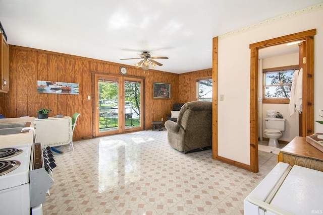 living area featuring healthy amount of natural light, a ceiling fan, wood walls, light floors, and baseboards