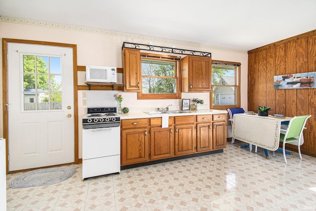 kitchen with white appliances, light countertops, a sink, brown cabinetry, and wooden walls