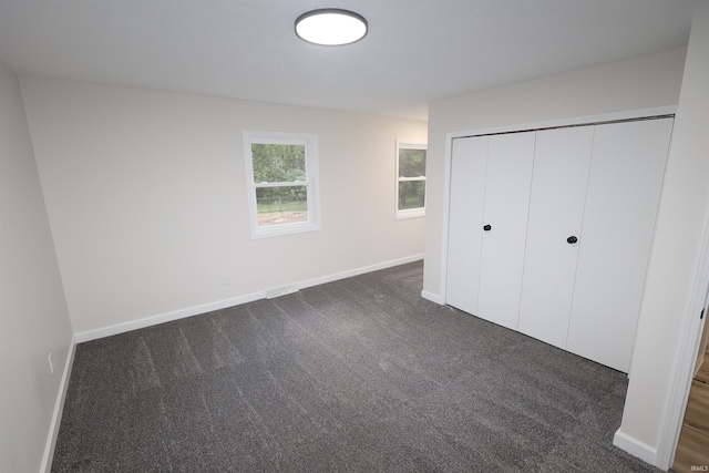 unfurnished bedroom featuring dark colored carpet, baseboards, and a closet