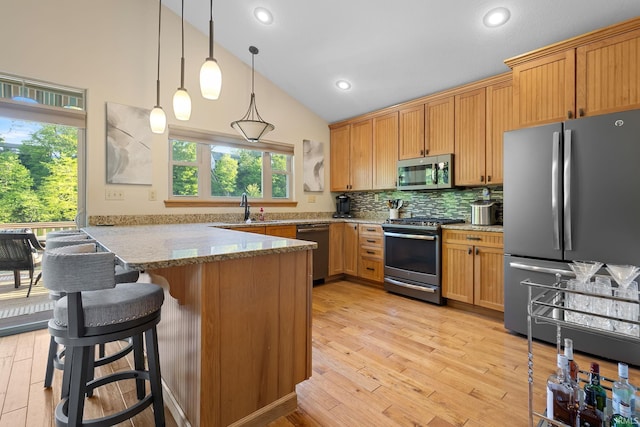 kitchen with appliances with stainless steel finishes, a peninsula, a sink, light stone counters, and plenty of natural light