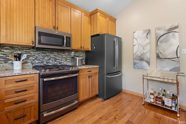 kitchen with appliances with stainless steel finishes, tasteful backsplash, light wood-style flooring, baseboards, and light stone countertops