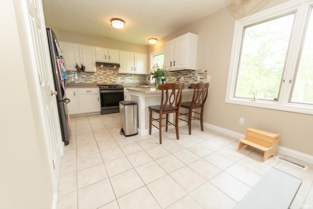 kitchen with stainless steel range oven, a peninsula, tasteful backsplash, and healthy amount of natural light