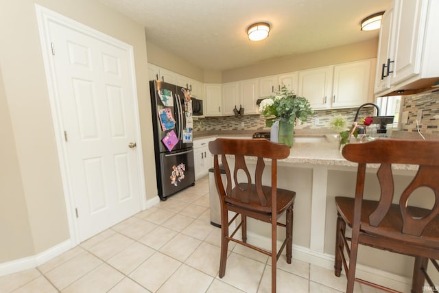 kitchen featuring freestanding refrigerator, a peninsula, backsplash, and white cabinetry
