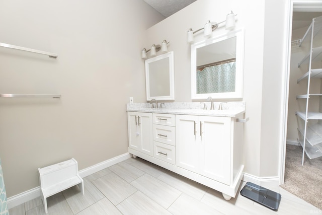 full bath with double vanity, a walk in closet, and baseboards