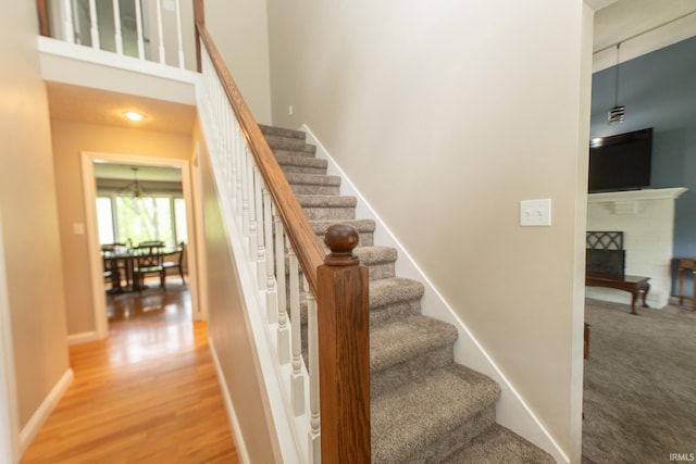 staircase featuring a fireplace, a high ceiling, wood finished floors, and baseboards