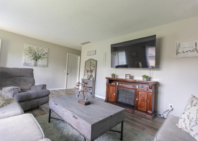 living room featuring wood finished floors, a glass covered fireplace, and baseboards