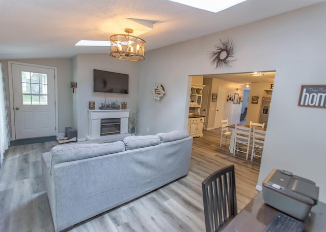 living area featuring a skylight, a glass covered fireplace, wood finished floors, vaulted ceiling, and a chandelier