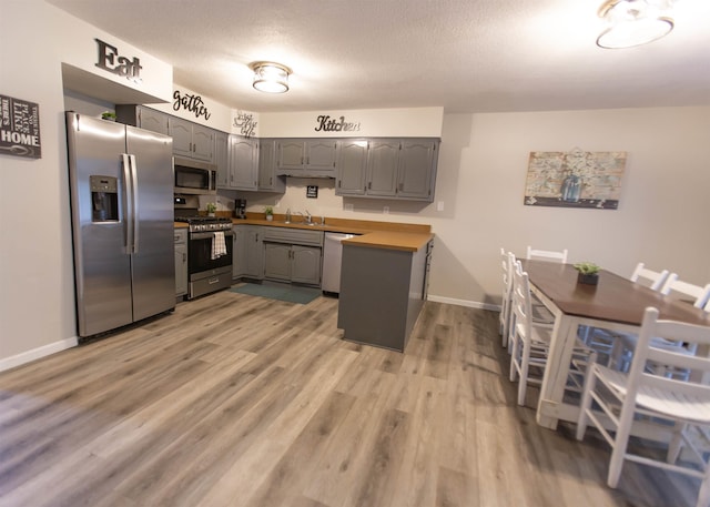kitchen featuring stainless steel appliances, gray cabinets, light wood-style flooring, baseboards, and a sink