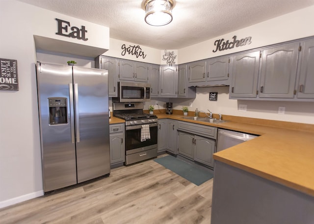 kitchen featuring stainless steel appliances, a sink, gray cabinets, a textured ceiling, and light wood-style floors