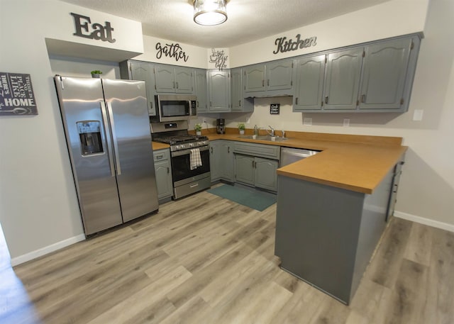 kitchen with stainless steel appliances, a sink, a peninsula, light wood-style floors, and baseboards