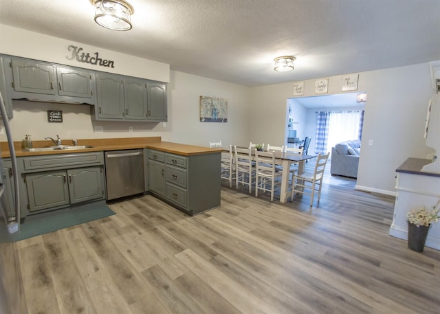 kitchen featuring stainless steel dishwasher, a sink, gray cabinets, light wood-type flooring, and a textured ceiling