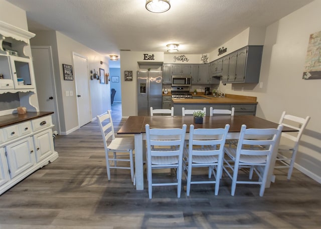kitchen featuring appliances with stainless steel finishes, baseboards, dark wood-type flooring, a peninsula, and gray cabinetry