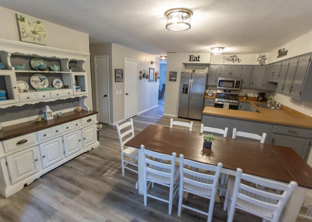 kitchen with appliances with stainless steel finishes, a sink, dark wood finished floors, a peninsula, and a textured ceiling