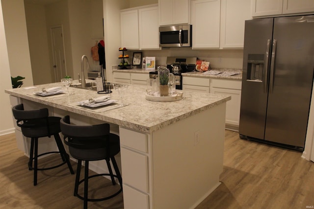 kitchen featuring appliances with stainless steel finishes, light wood-style flooring, white cabinetry, and a center island with sink