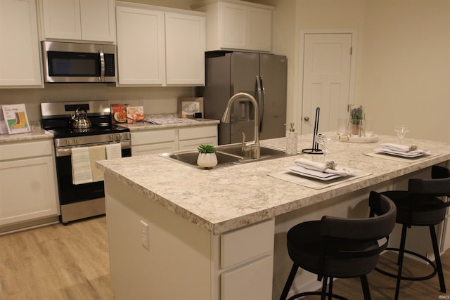 kitchen featuring stainless steel appliances, a sink, white cabinets, a breakfast bar, and light countertops
