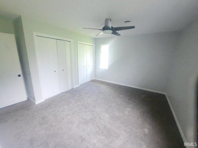 unfurnished bedroom featuring carpet, two closets, baseboards, and ceiling fan