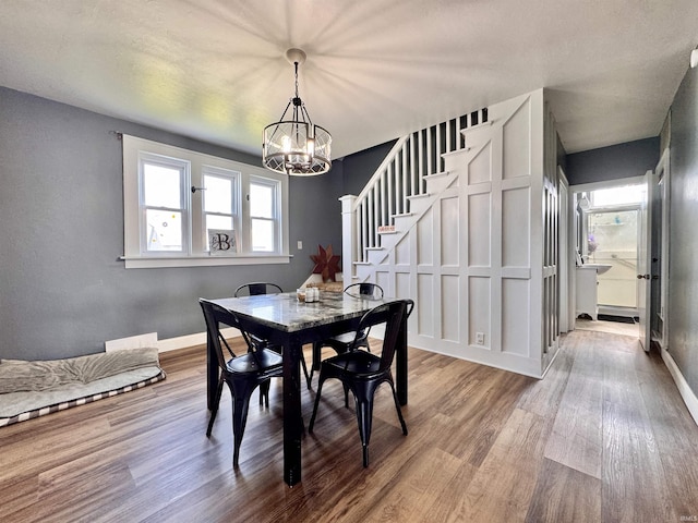 dining space with wood finished floors, a chandelier, stairs, and baseboards