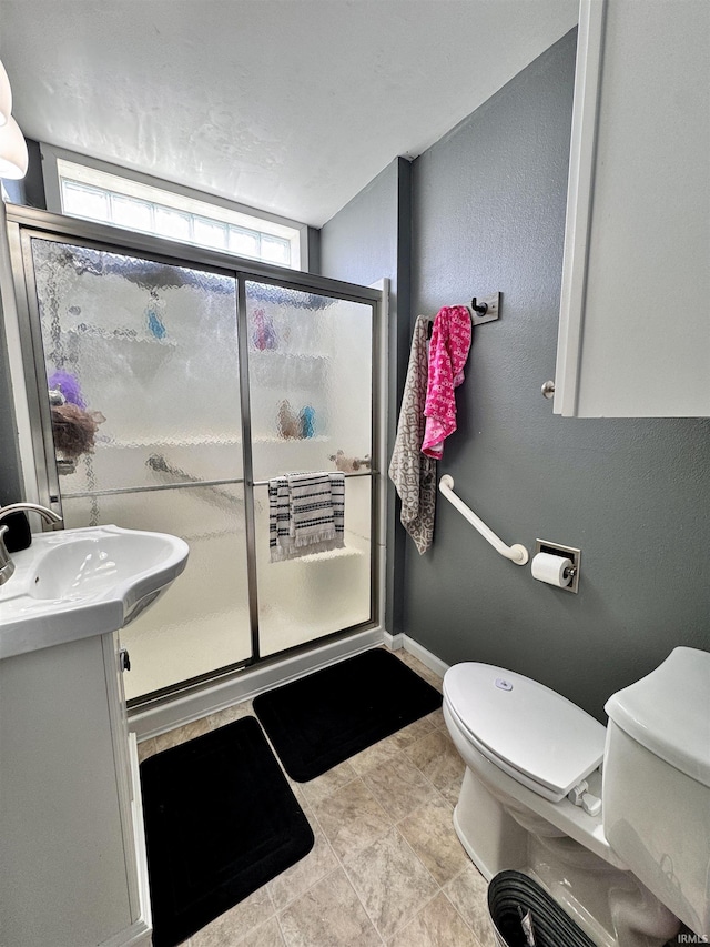 full bathroom featuring toilet, a stall shower, vanity, baseboards, and a textured wall