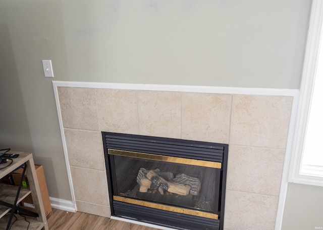 detailed view of a fireplace, wood finished floors, and baseboards