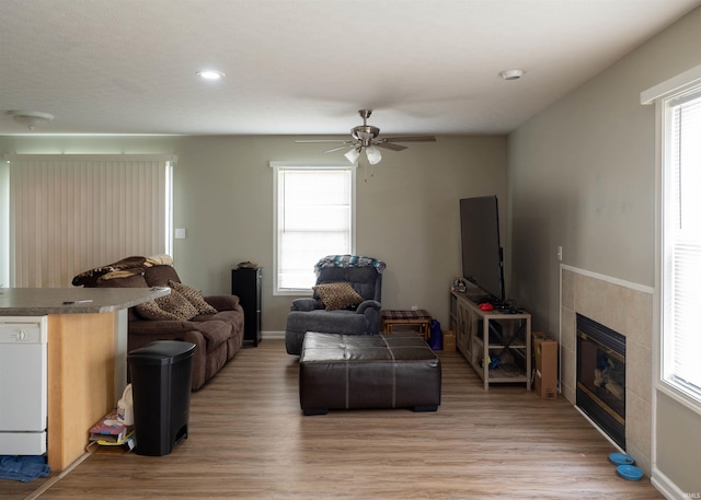 living room with light wood finished floors, a ceiling fan, a tile fireplace, recessed lighting, and baseboards