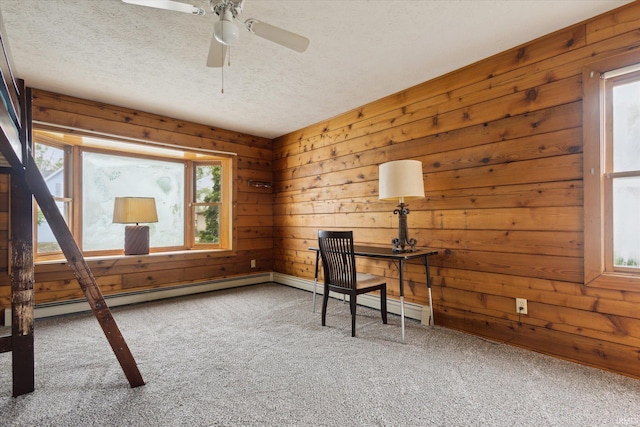 unfurnished office with carpet, a textured ceiling, wooden walls, a ceiling fan, and baseboard heating