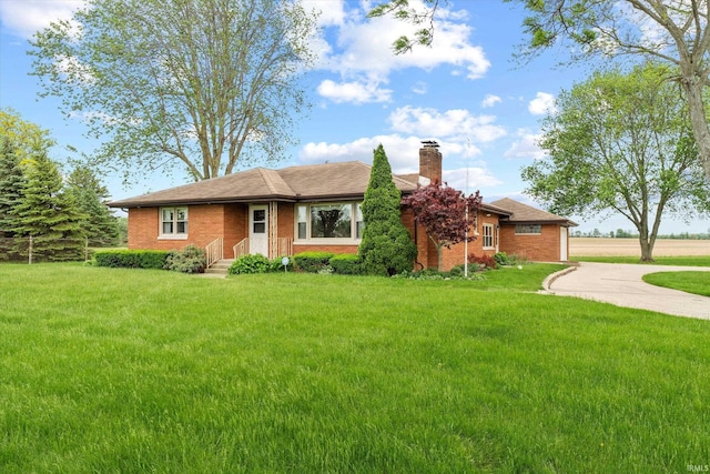 ranch-style home featuring a chimney, a front yard, driveway, and brick siding