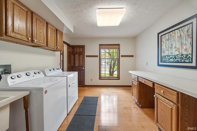 laundry room with cabinet space, washing machine and dryer, a textured ceiling, light wood finished floors, and baseboards
