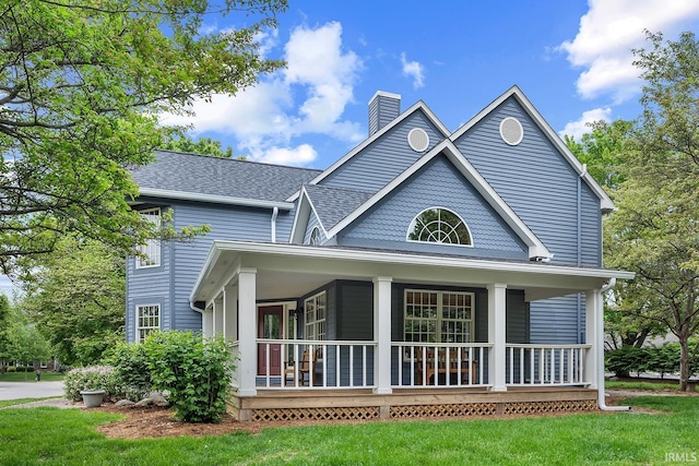 rear view of property with covered porch, a chimney, a lawn, and a shingled roof