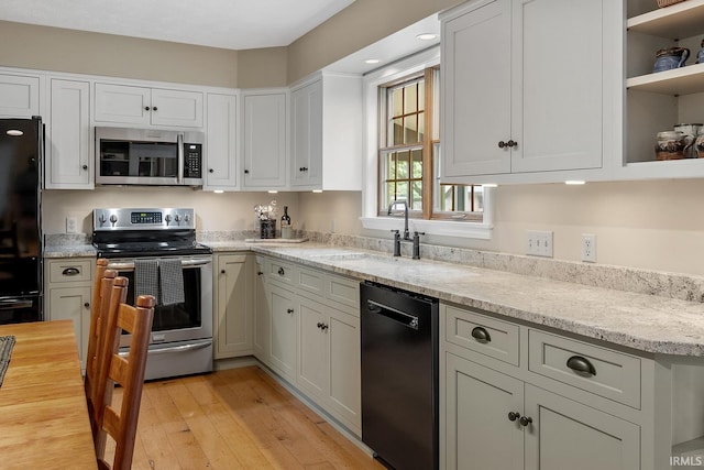 kitchen featuring black appliances, a sink, light wood-style floors, white cabinetry, and light stone countertops